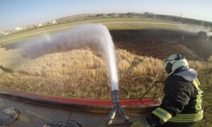 أحد عناصر الدفاع المدني السوري إلى جانب مضخة ماء فوق إحدى سيارات الإطفاء خلال إخماد أحد الحرائق الزراعية_ 30 من أيار 2022 (الدفاع المدني السوري/ فيس بوك)