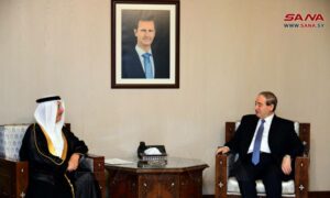 وزير الخارجية السوري فيصل المقداد إلى جانب سفير البحرين لدى سوريا وصورة بشار الأسد أعلى الجدار تفصل بينهما _ 9 من حزيران 2022 (سانا)