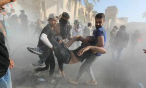 أشخاص يساعدون متظاهرًا مصابًا خلال اشتباكات مع قوات مكافحة الشغب بالقرب من مكتب رئيس الوزراء في بغداد- 30 آب 2022 (EPA)