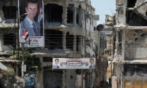 لافتات رئيس النظام بشار الأسد تتدلى من المباني التي دمرتها المعارك في مدينة حمص- (رويترز)