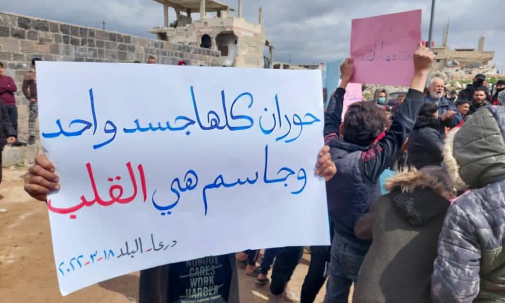 شاب من درعا البلد يحمل لافتة أمام المسجد العمري في إحياء الذكرى 11 للثورة السورية- آذار 2022 (تجمع أحرار حوران/ تويتر)