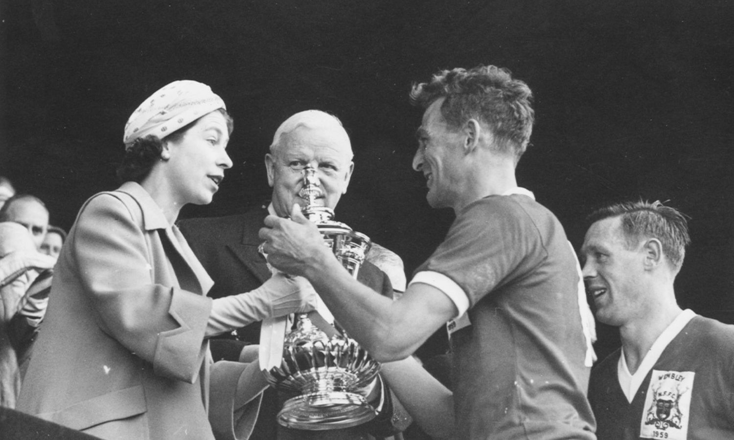 الملكة إليزابيث الثانية تقدم كأس الاتحاد الإنجليزي إلى قائد نادي نوتنجهام فورست لكرة القدم، جاك بوركيت، بعد فوز فريقه على لوتون تاون 2-1 في نهائي كأس الاتحاد الإنجليزي على ملعب ويمبلي بلندن- 2 من أيار 1959 (Paul Popper/ Getty Images)