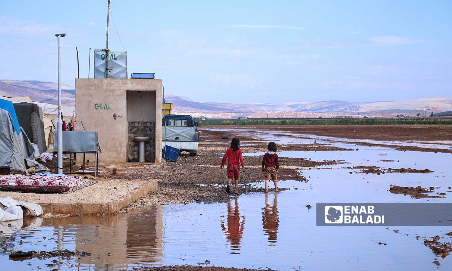 طفلان يمشيان  بالقرب من تجمع مياه الأمطار في مخيم السكة  بسهل الروج في ريف إدلب- 21 تشرين الأول 2022 (عنب بلدي/ محمد نعسان دبل)