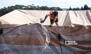 طفل يقوم بإفراغ سقف خيمة من المياه المتجمعة بفعل العاصفة المطرية التي ضربت منطقة سهل الروج في ريف إدلب- 21 تشرين الأول 2022 (عنب بلدي/ محمد نعسان دبل)