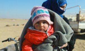 أم مع طفلها ينتظران حقيبة المساعدات الشتوية في أحد المخيمات بريف الرقة الشرقي - (UN)