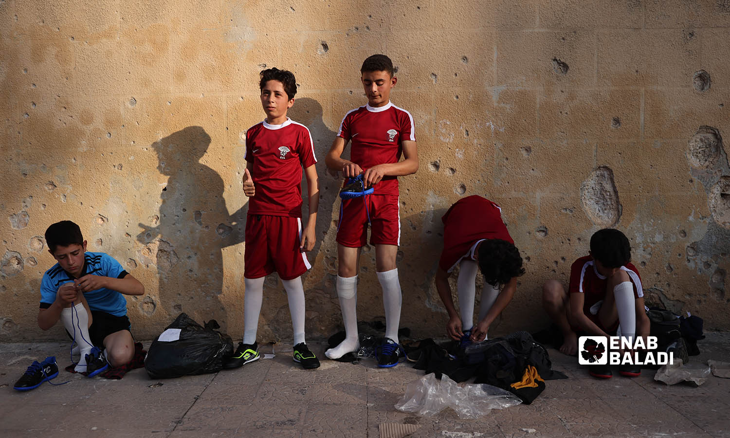 أطفال ناشئين يرتدون ملابسهم الرياضية على حيط مدمر في ملعب إدلب البلدي - 20 تشرين الثاني 2022 (عنب بلدي \ انس الخولي)