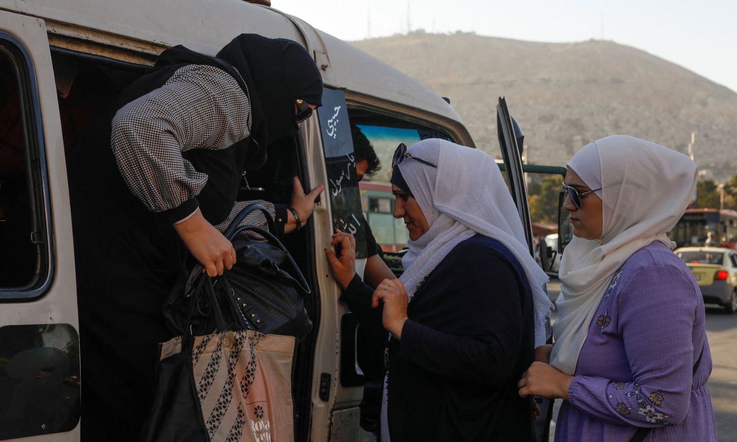 سيّدتان تتنظران نزول راكبة لتصعدا في ميكروباص في العاصمة السورية دمشق- 20 من تموز 2022 (رويترز)