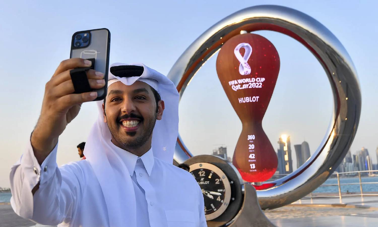 شخص يلتقط صورة شخصية أمام ساعة العد التنازلي الرسمية لكأس العالم في قطر 2022- كورنيش الدوحة (EPA)