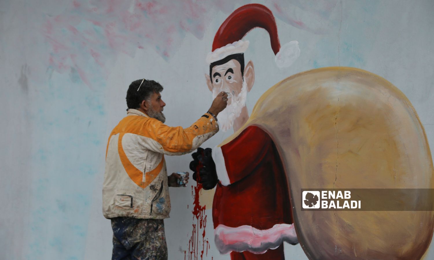 الرسام عزيز أسمر وأنيس حمدون، يرسمان جدارية بمناسبة رأس السنة الميلادية، تظهر بشار الأسد بشخصية بابا نويل وهو يوزع حبوب الكبتاجون في مدينة بنش - 25 كانون الأول 2022 (عنب بلدي / أنس الخولي)