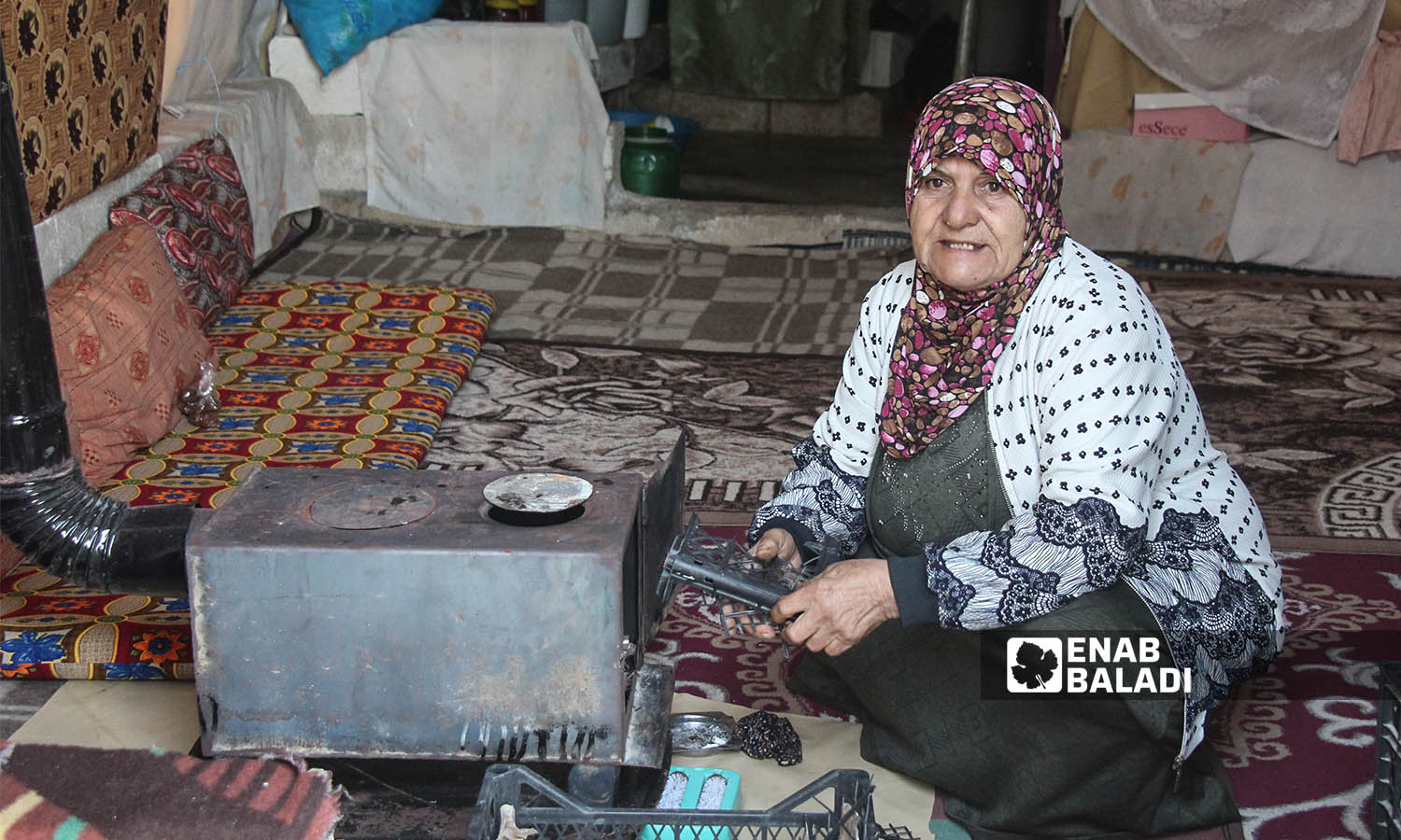 امرأة مسنة تشعل المدفأة بالبلاستيك في  خيمتها بمخيم خربة الجوز بريف إدلب قرب الحدود التركية- 23 من كانون الأول 2022(عنب بلدي/ إياد عبد الجواد)