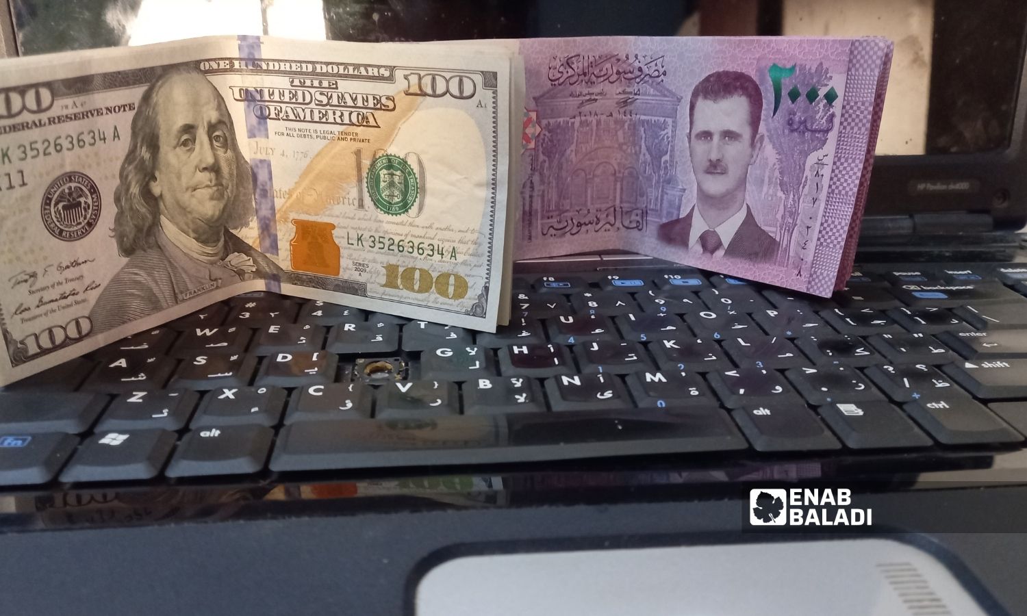 ورقة نقدية من فئة ألفي ليرة سورية إلى جانب 100 دولار أمريكي (عنب بلدي)