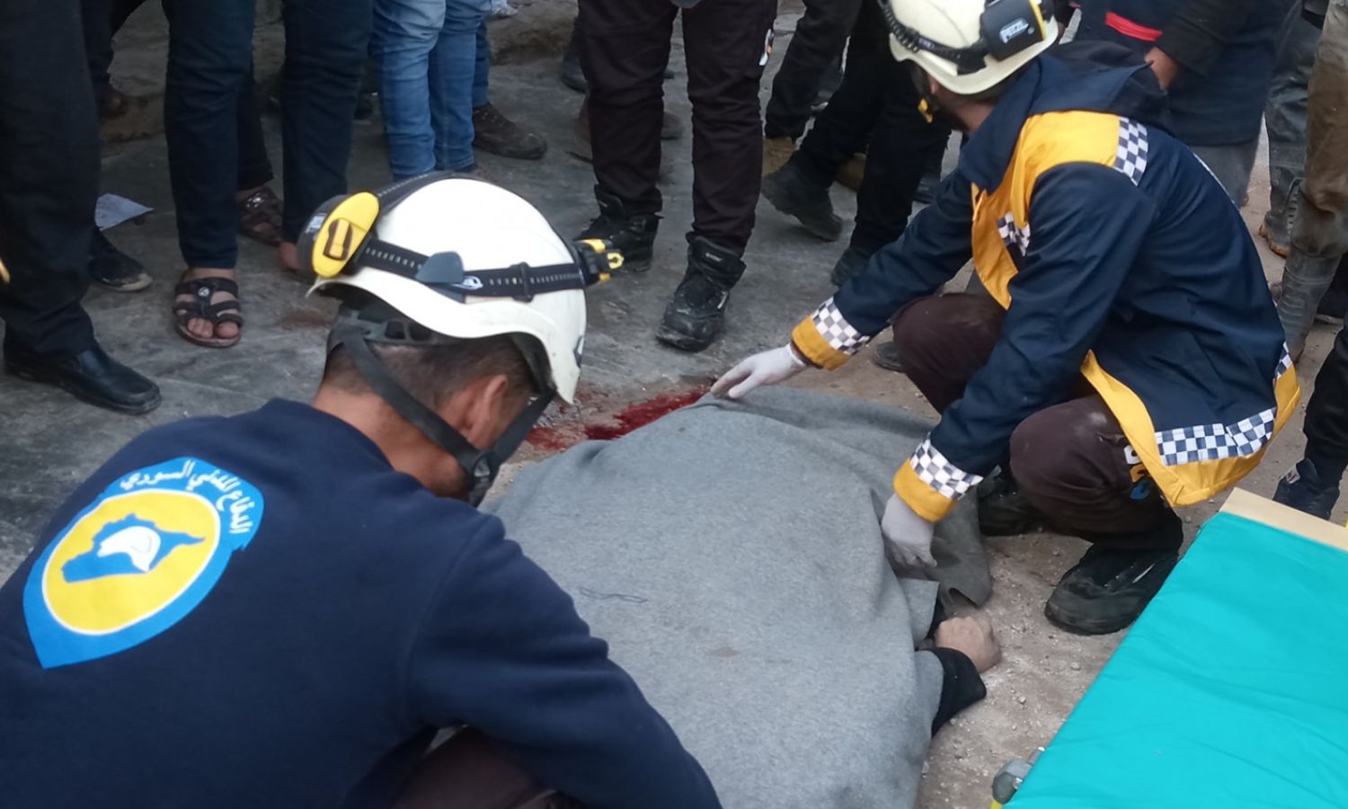 عنصران في "الدفاع المدني" ينقلان جثة امرأة توفيت دهسًا بسيارة مصفحة تركية (مدرعة)، في مدينة الأتارب بريف حلب الغربي- 5 من كانون الأول 2022 (ᎯᏰᎠᎯᏞᏞᎯᎻ ᎯᏞᏚᎻᏞᏫ/ فيس بوك)