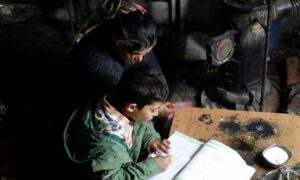 سيّدة سورية تساعد طفلها في دراسته قرب مدفأة مطأة (صوبيا)_ 30 من تشرين الثاني 2022 (رويترز)