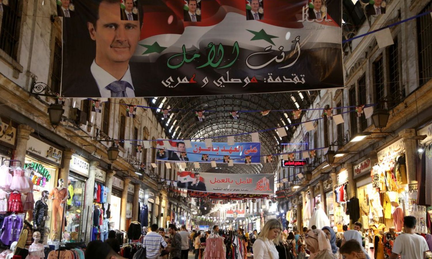 أشخاص يتجولون في سوق الحميدية في العاصمة دمشق وصور بشار الأسد تعلو الدكاكين_ 22 من أيار 2021 (رويترز)