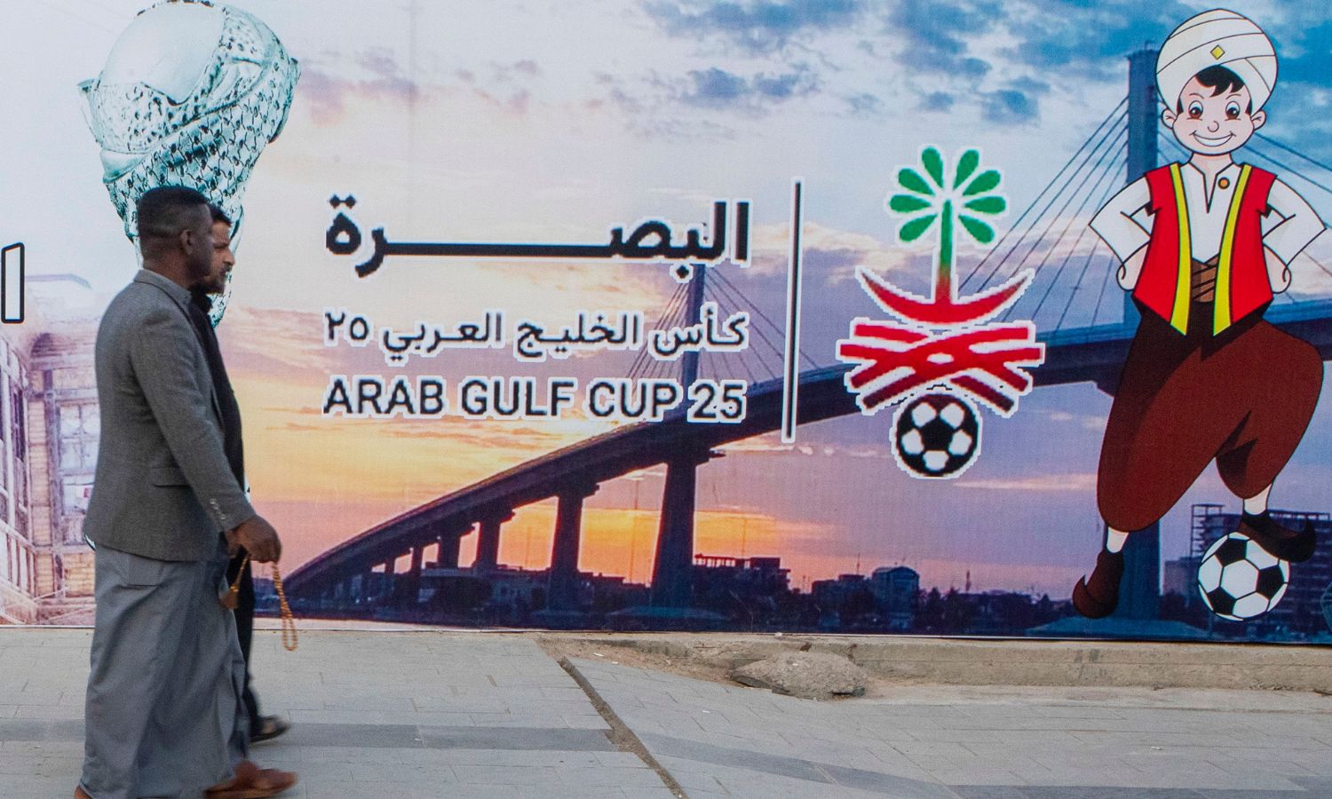 رجلان بالقرب من شعار بطولة "الخليج العربي" (خليجي 25) بمدينة البصرة العراقية- 3 كانون الثاني 2023 (AP)