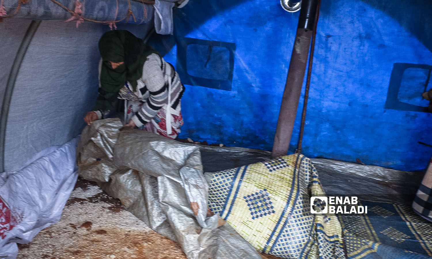 امراة تضع عازلًا على أرض خيمتها في مخيم النور بريف إدلب - 16 كانون الثاني 2023 (عنب بلدي/إياد عبد الجواد)