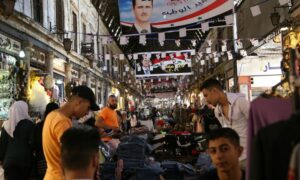 أشخاص يتسوقون في سوق الحميدية الذي ترتفع فيه صور رئيس النظام السوري بشار الأسد في العاصمة دمشق_ 22 من أيار 2021 (رويترز)
