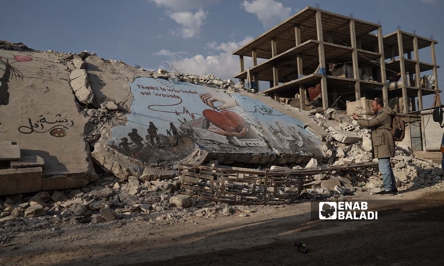 رجل يصور  رسومات جرافيتي فوق ركام الأبنية الذي دمرها الزلزال في مدينة جنديرس بريف حلب - 24شباط 2023 (عنب بلدي/ أمير خربطلي)