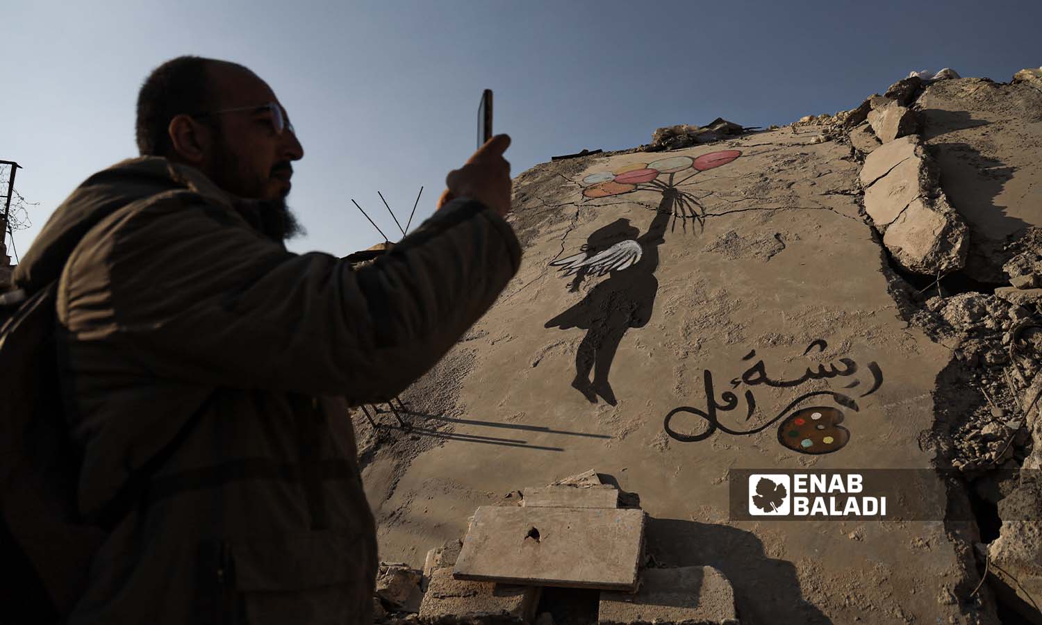 رجل يصور  رسومات جرافيتي فوق ركام الأبنية الذي دمرها الزلزال في مدينة جنديرس بريف حلب - 24شباط 2023 (عنب بلدي/ أمير خربطلي)