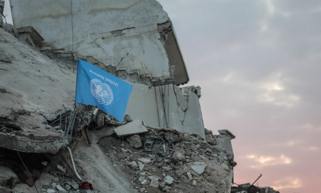 علم الأمم المتحدة وهو مقلوب أعلى ركام بناء مدمّر في بلدة جنديرس بريف حلب الشمالي استنكارًا لتأخر الاستجابة إثر زلزال ضرب مناطق تركيا وأربع سورية- 11 شباط 2023 (متداول/ وليد أكتع)