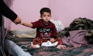 طفل سوري يجلس على سرير في مستشفى باب الهوى ويمسك بيد أمه بعد إصابته في الزلزال الذي وقع في بلدة حارم - 14 شباط 2023 (رويترز)