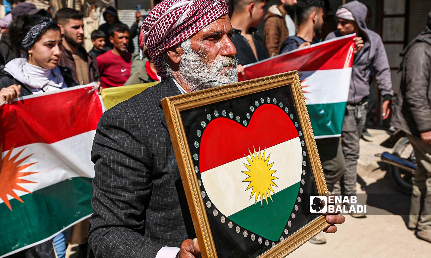 سوري كردي يحمل لوحة للعلم الكردي خلال تشييع أربعة مدنيين من الكرد قُتلوا خلال الاحتفال بعيد "نوروز" في مدينة جنديرس بريف حلب الشمالي- 21 من آذار 2023 (عنب بلدي/ أمير خربوطلي)