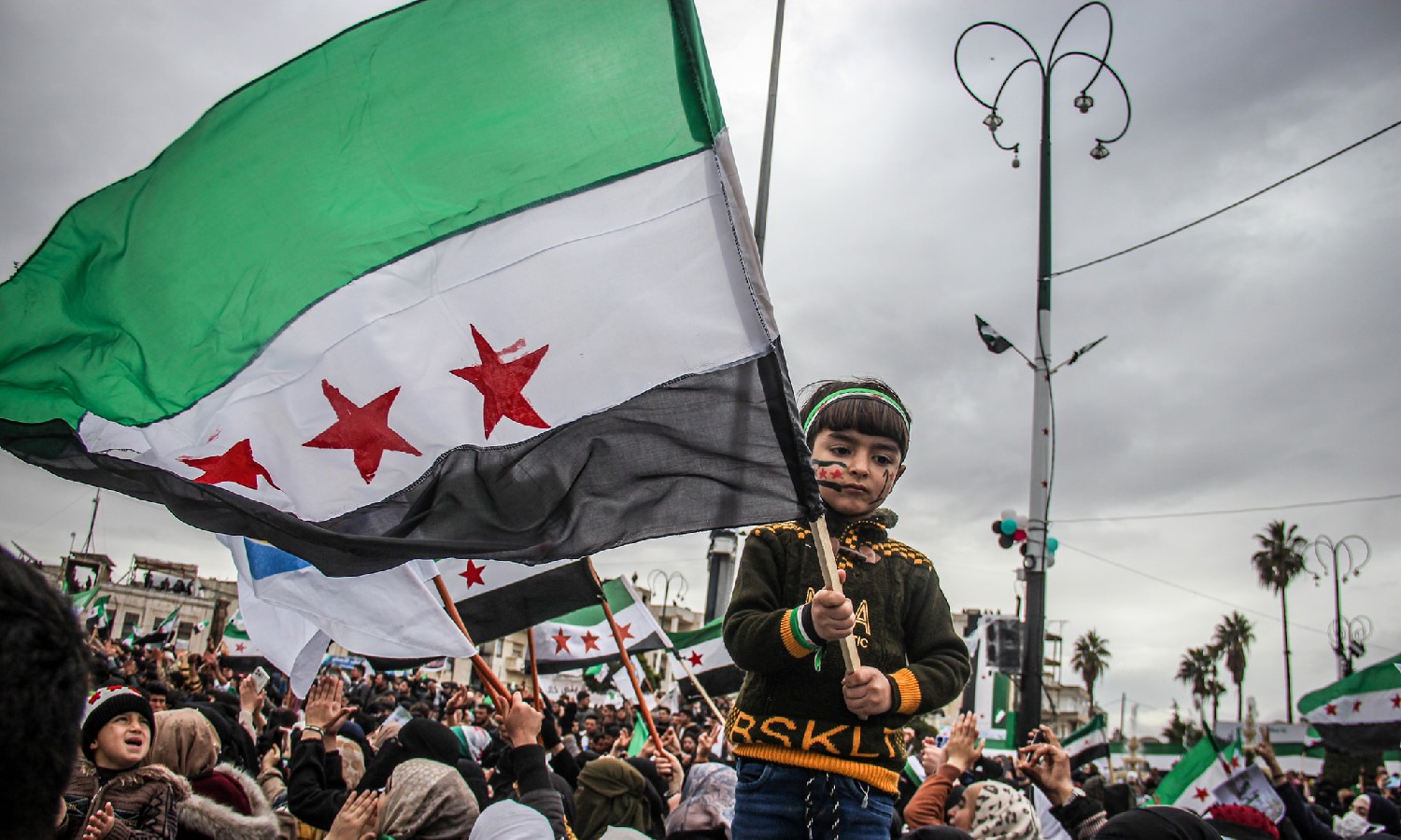 طفلة تحمل علم الثورة السورية خلال مظاهرة في مدينة إدلب لإحياء الذكرى الـ12 للثورة في سوريا- 15 من آذار 2023 ( Mohamad Kazmooz/ فيس بوك)