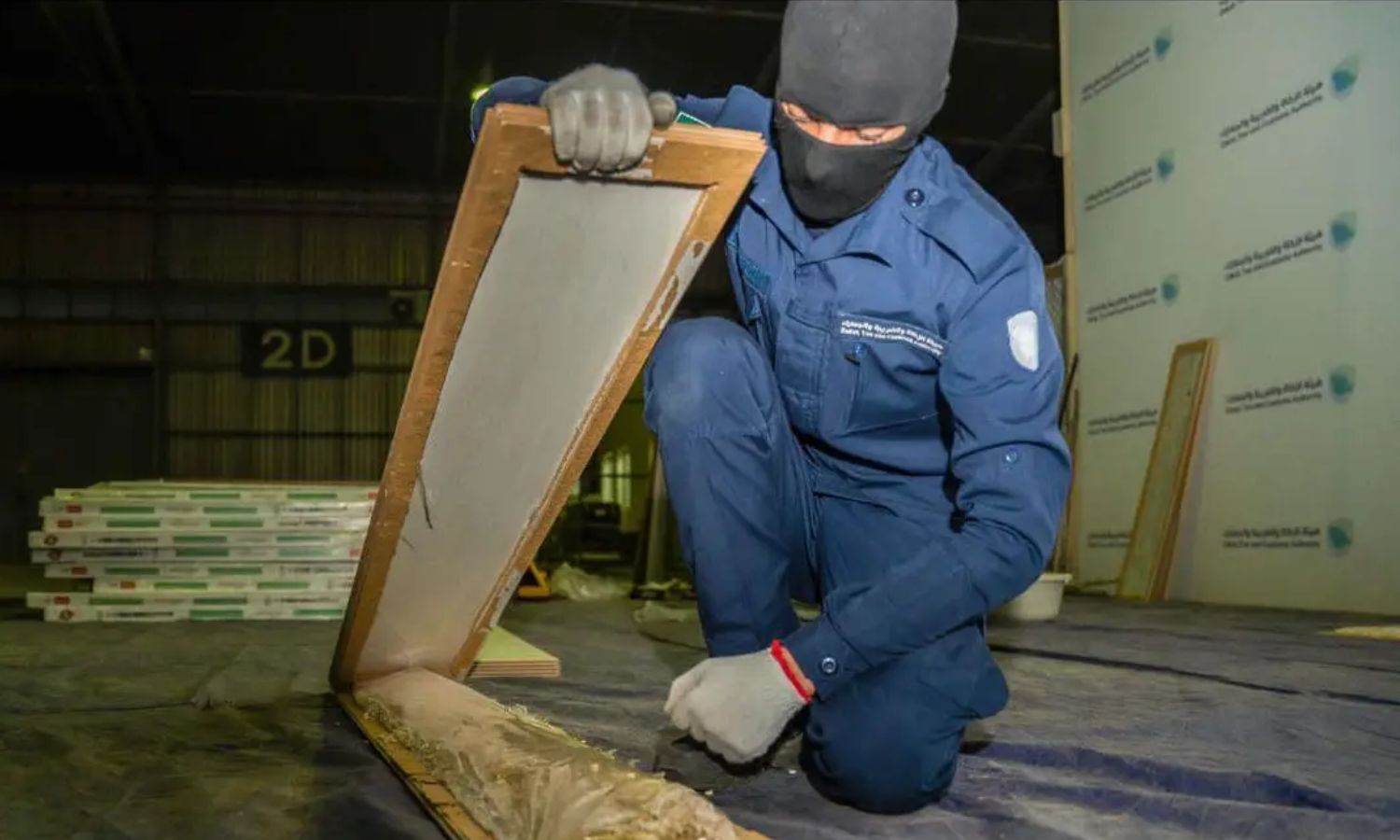 عنصر من هيئة الزكاة والضريبة والجمارك السعودية يفتح لوحًا خشبيًا يحتوي أقراًا مخدرة خلال محاولة تهريب شحنة إلى السعودية عبر ميناء جدة الإسلامي- 15 من أيار 2023 (واس)