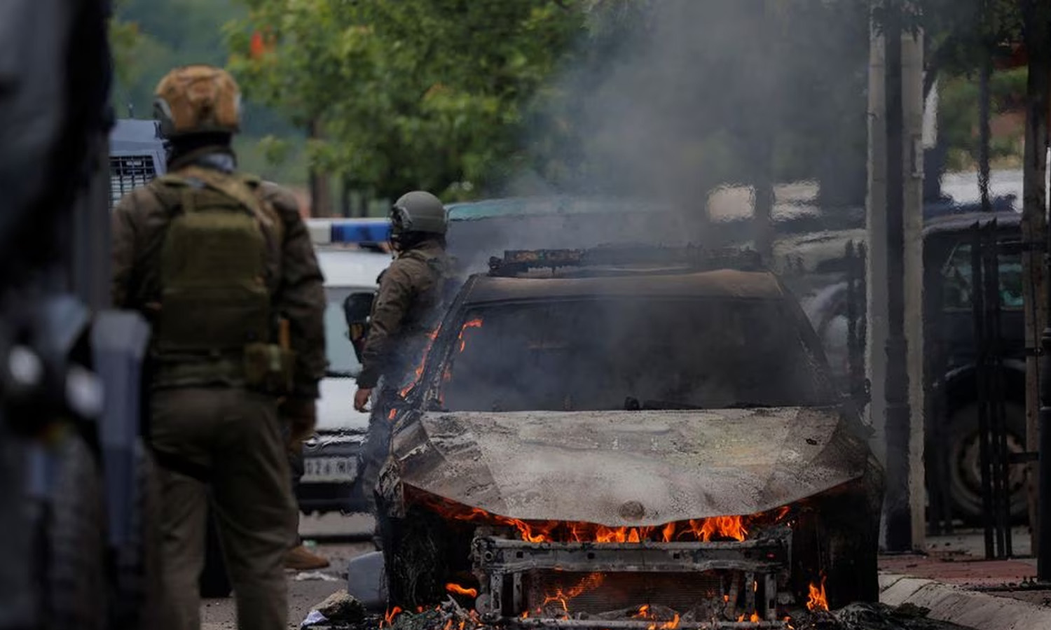 ضباط من قوات الشرطة الخاصة يقفون بجوار سيارة محترقة بعد اشتباكات بين شرطة كوسوفو ومتظاهرين صرب حاولوا منع العمدة المنتخب حديثًا من أصل ألباني من دخول مكتبه سمالي البلاد- 26 أيار 2023 (رويترز)