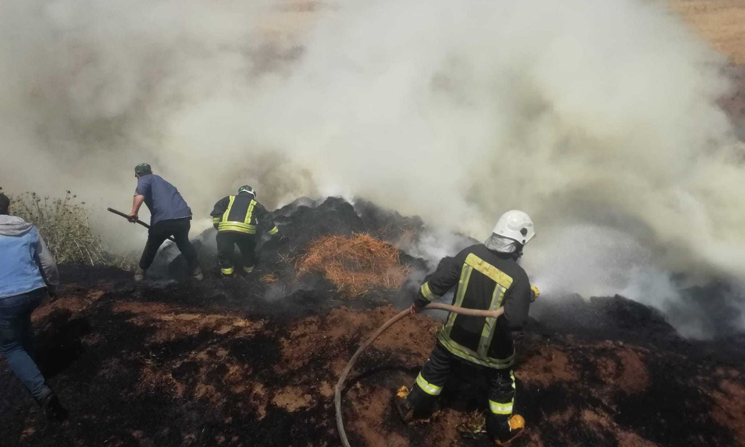 متطوعان في "الدفاع المدني السوري" وأهالي يخمدون حريقًا اندلع في الأراضي الزراعية شمال غربي سوريا- 22 من أيار 2023 (الدفاع المدني السوري/ فيس بوك)