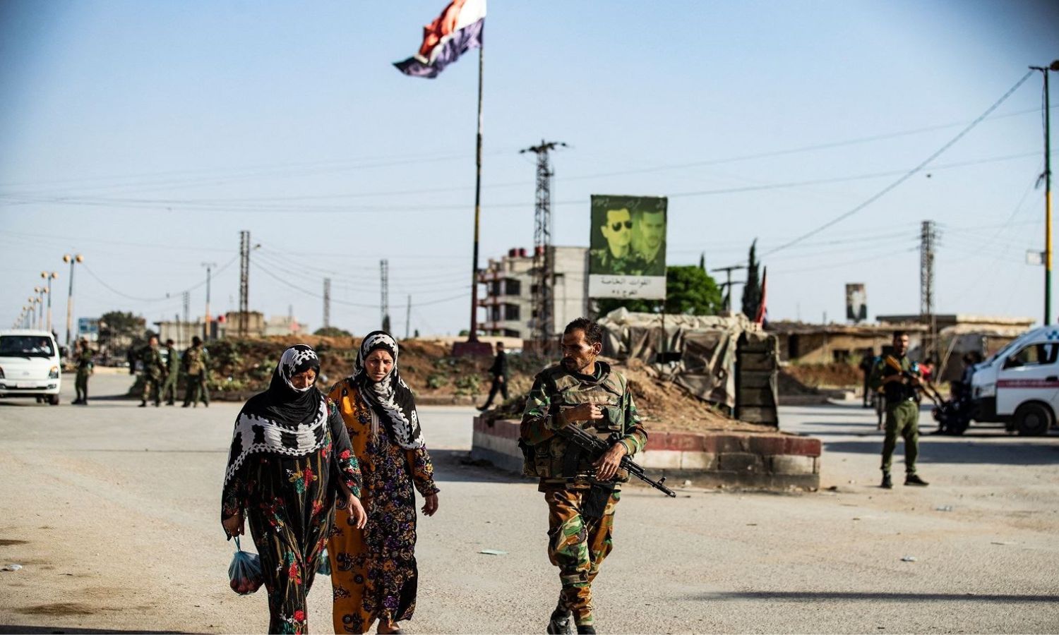 عنصر من قوات النظام السوري يسير بجانب سيدتين قرب حاجز عسكري قرب مدينة القامشلي شمال شرقي سوريا- 27 من نيسان 2021 (AFP)