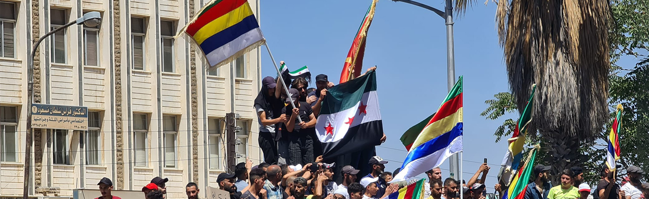 أهالي السويداء خلال احتجاجات ساحة السير وسط المدينة يرفعون راية الثورة السورية بجانب راية الموحدون (الحدود الخمسة) - 24 من آب 2023 (السويداء 24)