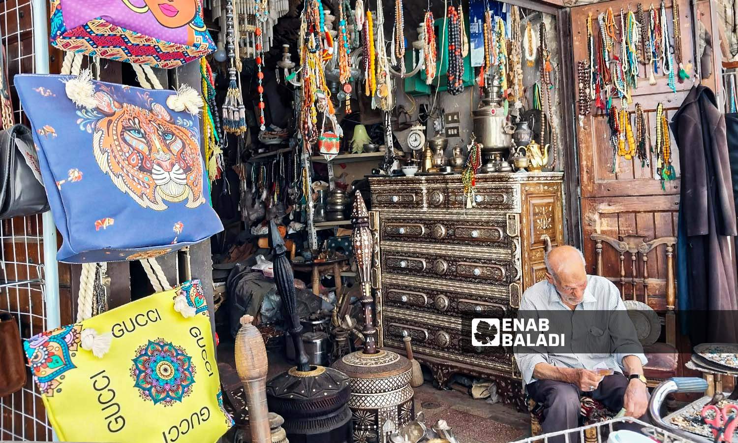 رجل مسن يجلس أمام محل لبيع التحف والتذكارات  بحي القيمرية في دمشق - 26 من تموز 2023 (عنب بلدي / سارة الأحمد)
