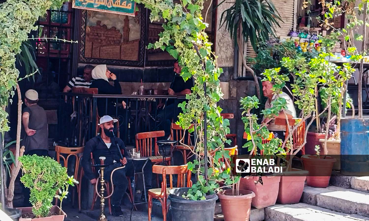رجال ونساء يجلسون في قهوة النوفرة بحي القيمرية في دمشق - 26 من تموز 2023 (عنب بلدي / سارة الأحمد)

