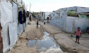 أطفال لاجئون يقفون قرب مجرى مياه مكشوف في مخيم غير رسمي في وادي البقاع اللبناني- 18 من كانون الأول 2023 (رويترز)