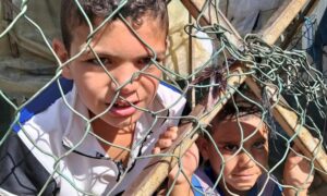 أطفال لاجئون سوريون ينظرون من خلف سياج في مخيم غير رسمي في عكار بلبنان- 19 من تشرين الأول 2021 (رويترز)