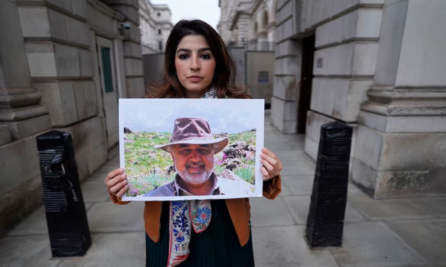 روكسان طهباز تحمل صورة والدها مراد طهباز، المعتقل في إيران، خلال احتجاج في لندن 2022 (AFP)