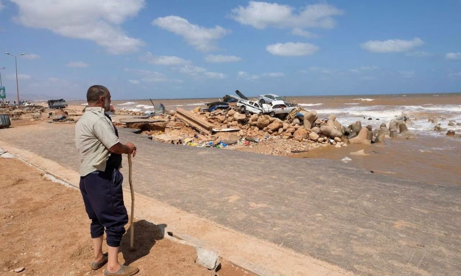 رجل يقف بعد العاصفة في مدينة درنة الليبية ينظر إلى السيارات المتضررة نتيجة العاصفة -12 من أيلول 2023 (رويترز)