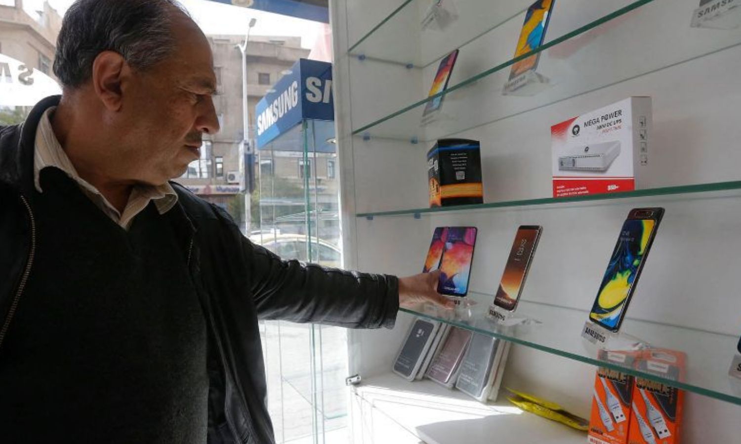 رجل يتفحص الهواتف المحمولة الذكية في محل هواتف بالعاصمة السورية - 24 من آذار 2021 (AFP)