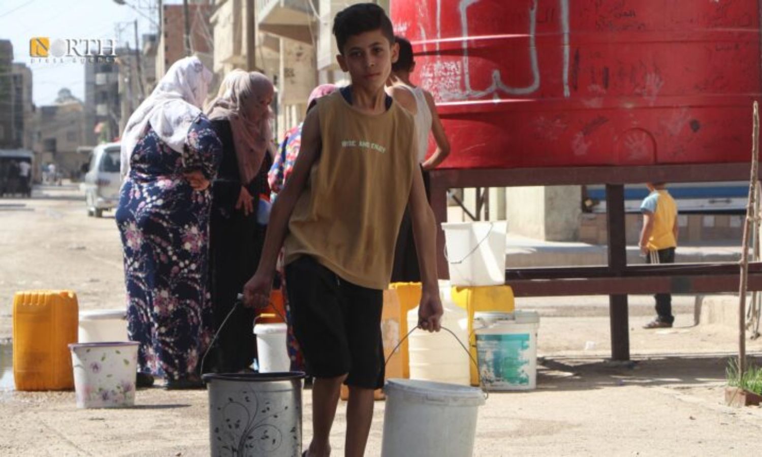 طفل ومن خلفه سكان يسعون للحصول على مياه الشرب في حي غويران بالحسكة- 5 من حزيران 2023 (نورث برس)