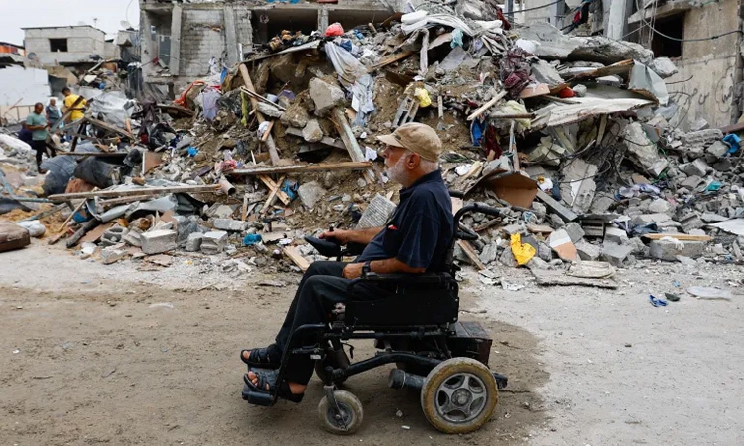 فلسطيني على كرسي متحرك يمر بالقرب من أنقاض المباني التي دمرتها الهجمات الإسرائيلية في رفح بجنوب قطاع غزة - 9 تشرين الأول 2023 (إبراهيم أبو مصطفى/رويترز)