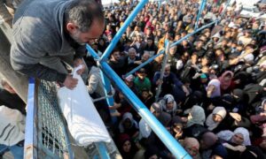 رجل فلسطيني يحمل كيسًا من الطحين والكثيرون ينتظرون استلامه خلال فترة الهدنة المؤقتة بين 
