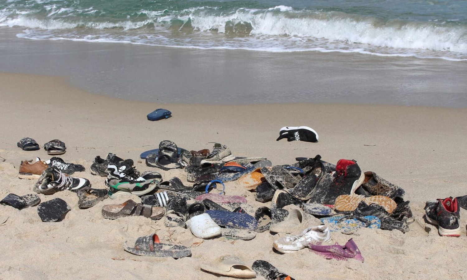 أحذية المهاجرين على الشاطئ في قصر الخيار ليبيا، بعد انقلاب قاربهم- في 15من  شباط 2023 (رويترز)