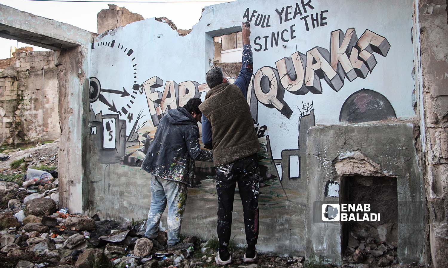 فريق ريشة أمل يرسم جدارية في بنش على جدران احد المنازل المتضررة من الزلزال الذي ضرب شمال غربي سوريا - 6 من شباط 2024 (عنب بلدي/ عبد الكريم الثلجي)
