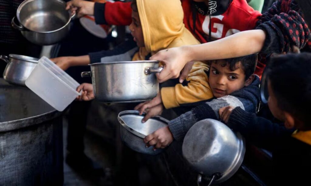 أطفال فلسطينيون ينتظرون الحصول على الطعام في ظل نقص الإمدادات الغذائية الإغاثية عن قطاع غزة، واستمرار الحرب الإسرائيلية على القطاع- 5 من آذار 2024 (رويترز)