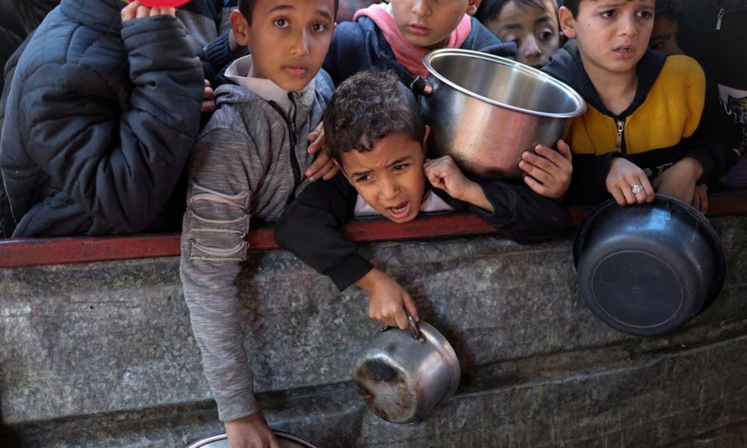 أطفال فلسطينيون ينتظرون الحصول على الطعام المطبوخ في مطبخ خيري وسط نقص الإمدادات الغذائية، ومع استمرار الصراع المستمر بين إسرائيل وحركة "حماس" في رفح، جنوب قطاع غزة- من شباط 2024 (رويترز)