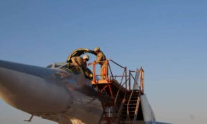 طيارون روس يتعاملون طائرة حربية روسية في قاعدة حميميم الجوية بريف محافظة اللاذقية على الساحل السوري (سبوتنيك)
