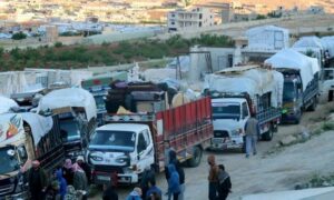 لاجئون سوريون يقفون بالقرب من شاحنات تحمل أمتعتهم ويستعدون لمغادرة لبنان إلى سوريا، في عرسال بوادي البقاع، في 14 من أيار 2024 (AFP)