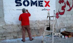 خطاط يكتب لوحة إعلانية على جدار قرب شارع "الكورنيش" في القامشلي - 8 من أيار 2024 (عنب بلدي/ مجد السالم)
