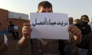 طفل يحمل لافتة في مظاهرة بمخيم الركبان شرقي سوريا بالقرب من الحدود الأردنية- 11 من أيار 2024 (صفحة المخيم على فيس بوك)